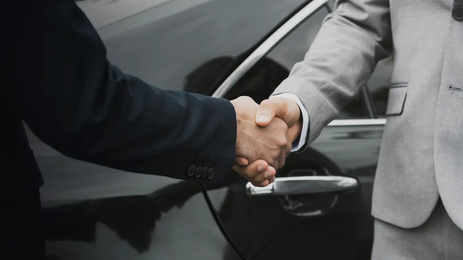 Dos hombres sellan un trato dándose la mano delante de un coche negro